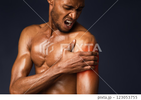Sports Injury. Shirtless afro man suffering from pain in shoulder, touching hand with red zone, black wall, copyspace Sports Injury. Shirtless afro man suffering from pain in shoulder, touching hand with red zone, black wall, copyspace 123053755
