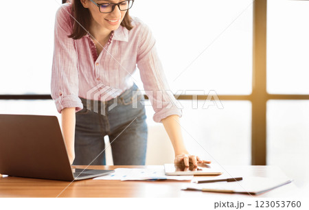 Office Work. Beautiful female manager in glasses standing at desk using laptop and touching tablet, copyspace 123053760