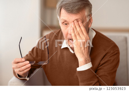Glaucoma. Tired Elderly Man Massaging Eye Holding Eyeglasses Having Eyestrain And Ocular Tension Sitting On Couch At Home. Selective Focus 123053923