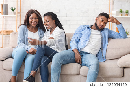 Third wheel. Bored african american guy sitting on sofa next to two girlfriends taking selfie, copy space 123054150