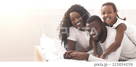 Happy together. African american parents and their daughter lying on bed and using laptop, browsing internet or watching movie Happy together. African american parents and their daughter lying on bed and using laptop, browsing internet or watching movie 123054259