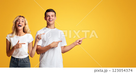 Joyful young guy and girl pointing away at copy space on yellow background Joyful young guy and girl pointing away at copy space on yellow background 123054374