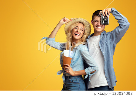 Ready for travel. Happy millennial couple holding passport with tickets and retro photocamera over yellow studio background with free space Ready for travel. Happy millennial couple holding passport with tickets and retro photocamera over yellow studio background with free space 123054398