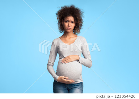 Tired pregnant woman embracing her belly and looking at camera, grey background 123054420