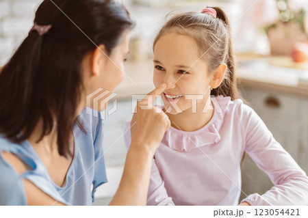 A mother and her young daughter are playing a game where they touch each others noses. The girl is smiling and looking at her mother with happiness. They appear to be in their kitchen A mother and her young daughter are playing a game where they touch each others noses. The girl is smiling and looking at her mother with happiness. They appear to be in their kitchen 123054421