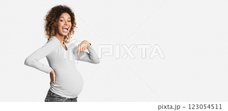Overjoyed black pregnant woman pointing at her belly over white studio background 123054511