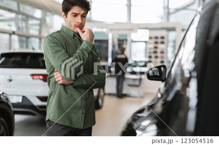 Pensive young guy thinking, making choice, having doubt about buying new car at dealership centre, copy space. Thoughtful millennial Caucasian man selecting auto at showroom store 123054516