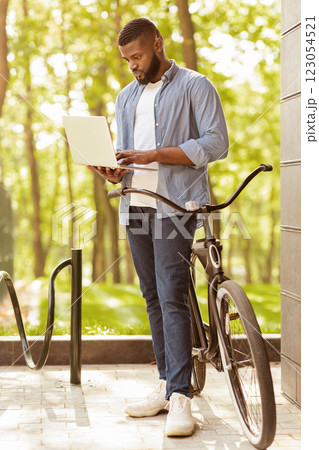 Freelance Job. Millennial Afro Guy Standing Near His Bicycle And Working On Laptop Outdoors, Finishing Project, Vertical Full-Length Photo 123054521