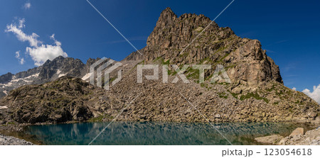 Clear mountain lake reflecting rugged cliffs and snow capped peaks in alpine landscape Clear mountain lake reflecting rugged cliffs and snow capped peaks in alpine landscape 123054618