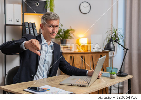 Upset young Caucasian freelancer in suit using laptop and showing thumb down at home office table 123054718
