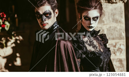 A man and a woman are standing next to each other. The man is wearing a black suit jacket and a dark red cape. The woman is wearing a black lace dress 123054881