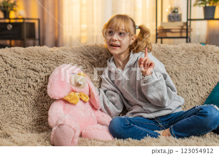 Young teenager child girl happily talking to plush bunny at home sofa pretend fun imaginative vibes Young teenager child girl happily talking to plush bunny at home sofa pretend fun imaginative vibes 123054912