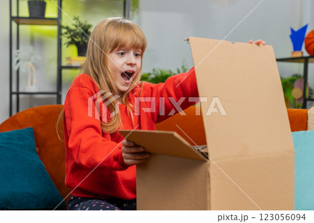 Happy child girl shopper unpacking cardboard box delivery parcel online shopping purchase at home Happy child girl shopper unpacking cardboard box delivery parcel online shopping purchase at home 123056094