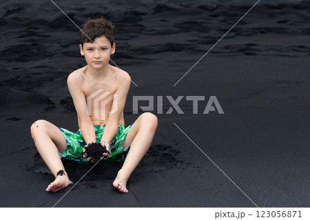 Teen boy is sitting on the Black sand beach in Hawaii. 123056871