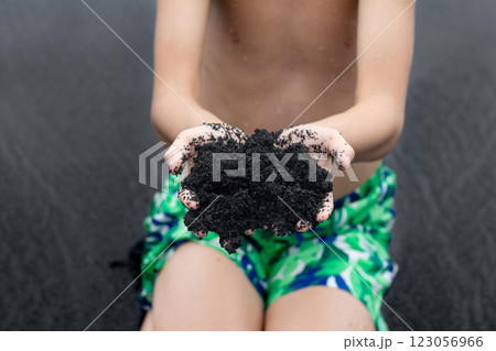 Teenager is holding a handful of black sand in Hawaii beach. 123056966
