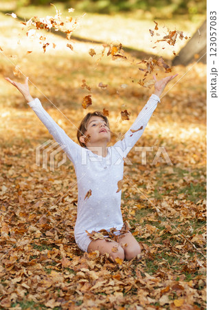 Girl is sitting on the ground in the fall park and throwing yellow leaves. 123057083