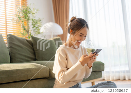 Happy young asian woman relax on comfortable couch at home texting messaging on smartphone Happy young asian woman relax on comfortable couch at home texting messaging on smartphone 123058627