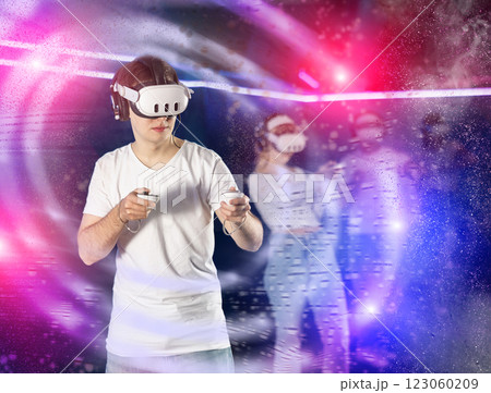 In darkened hall of gaming club, guy in VR helmet takes part in group game, visual special effects In darkened hall of gaming club, guy in VR helmet takes part in group game, visual special effects 123060209
