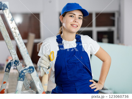 Positive young female builder in blue workwear standing at construction site Positive young female builder in blue workwear standing at construction site 123060736