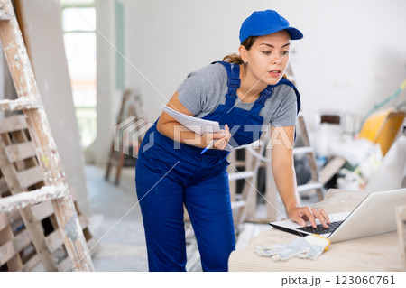Portrait of a female builder who checks the work done using laptop 123060761
