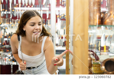 Enthusiastic young girl looking at artisanal copper utensils in souvenir shop 123060782