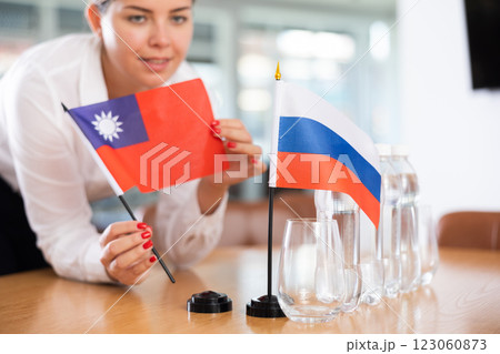 Young woman putting flags of Taiwan and Russia on table in office 123060873