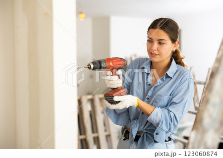Woman builder using drill to bore hole in wall 123060874