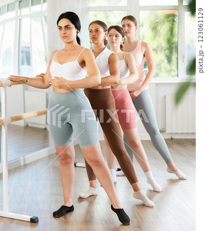 Young woman practicing battement tendu holding by ballet barre together with others 123061129