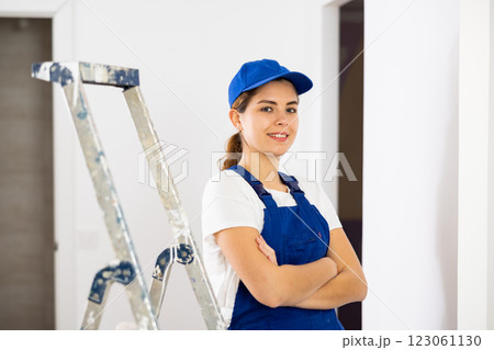 Portrait of contented young female builder in blue overalls during the repair of cottage 123061130