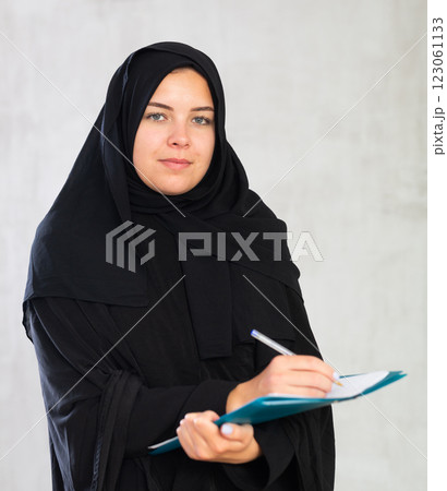 Cheerful young muslim student in black traditional hijab with notebooks in hands 123061133