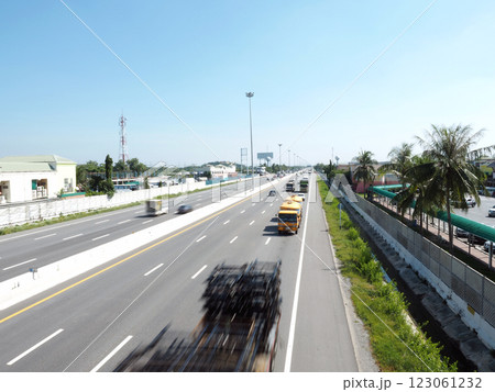 A busy highway scene with vehicles in motion, surrounded by greenery and buildings. clear blue sky adds to vibrant atmosphere A busy highway scene with vehicles in motion, surrounded by greenery and buildings. clear blue sky adds to vibrant atmosphere 123061232