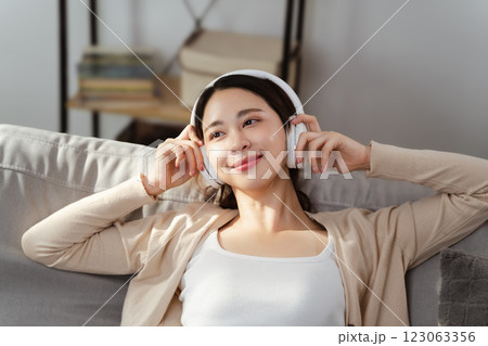 A beautiful young woman wearing headphones is listening to music, feeling happy, and relaxed. 123063356