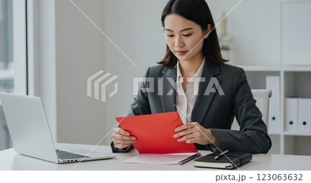 Businesswoman in suit reading document at desk with laptop and notebooks 123063632