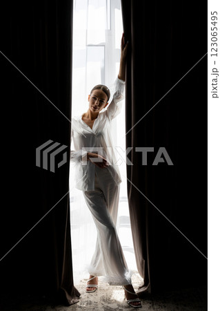Bride opening curtains in white silk pajamas on wedding day Bride opening curtains in white silk pajamas on wedding day 123065495