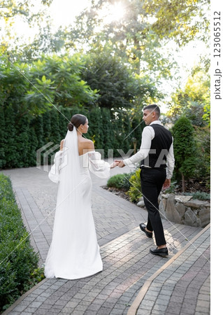 Groom tenderly embracing bride while holding hands in park during wedding ceremony Groom tenderly embracing bride while holding hands in park during wedding ceremony 123065512