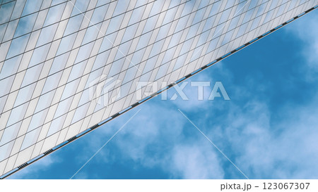 A sleek, angled building with a reflective, grid-like glass facade dominates the left, contrasting against a vibrant blue sky with soft white clouds. A sleek, angled building with a reflective, grid-like glass facade dominates the left, contrasting against a vibrant blue sky with soft white clouds. 123067307