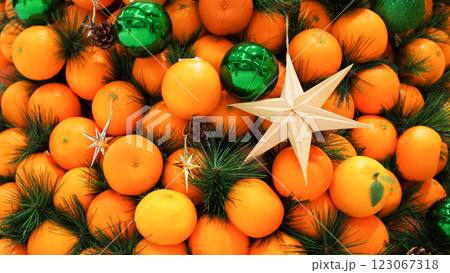 A decorative arrangement of fresh oranges, pine branches, green baubles, and star ornaments, blending natural and festive elements in a vibrant holiday display. 123067318