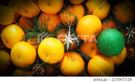 A festive arrangement of bright oranges, green pine branches, and Christmas ornaments, including a glittery green bauble and silver star, creating a vibrant holiday display. A festive arrangement of bright oranges, green pine branches, and Christmas ornaments, including a glittery green bauble and silver star, creating a vibrant holiday display. 123067319