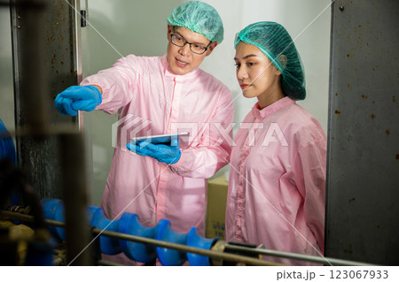 Two machine engineers at the beverages factory discuss quality control using a digital tablet. They focus on examining manufacturing processes in the drinks production plant. 123067933