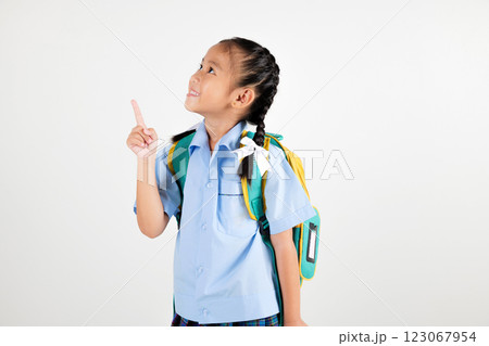 Portrait smiling Asian little girl kindergarten with schoolbag pointing finger at copy space studio shot isolated white background, happy woman kid in pigtails wearing school uniform, back to school 123067954