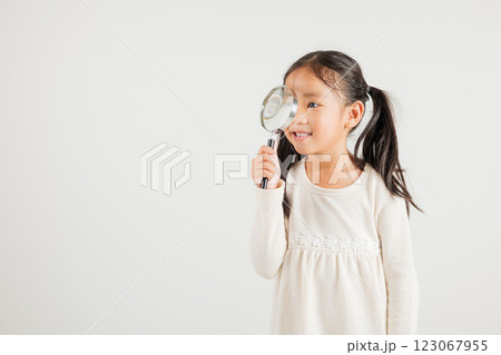 Asian little kid girl funny looking through magnifying glass at studio shot isolated on white background, Happy kindergarten child lifestyle smiling exploring holding magnifier searching, Education 123067955