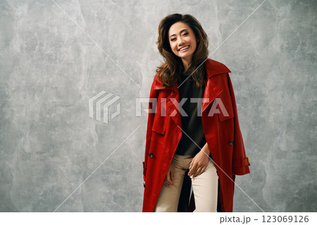 Stylish fashion woman in red coat and trendy casual outfit posing on grey background 123069126