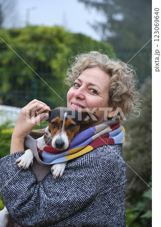Smiling woman holding small dog wrapped in scarf outdoors 123069640