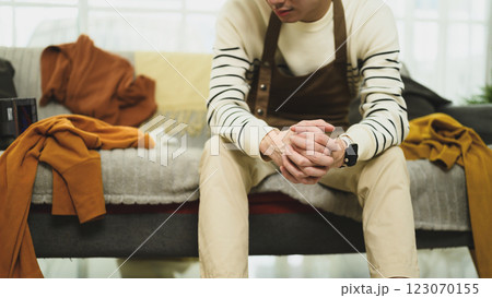 Young man sitting on the edge of a messy couch and looking exhausted 123070155