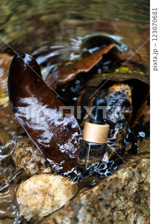 Serum bottle rests on rocks, surrounded by wet leaves and flowing water, creating a calm atmosphere. 123070681
