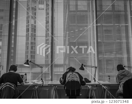 Students study in a modern urban workspace with large windows overlooking a cityscape on a busy Students study in a modern urban workspace with large windows overlooking a cityscape on a busy 123071348
