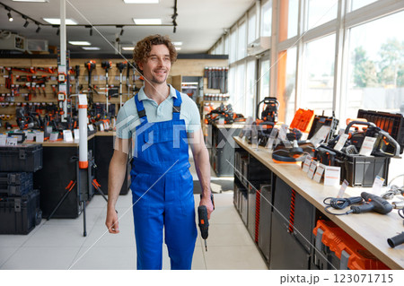Workman wearing coveralls walking with new drill among hardware store showcase 123071715
