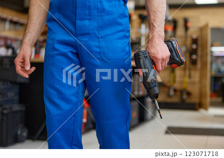 Crop portrait of repairman holding drill in hands over workshop interior Crop portrait of repairman holding drill in hands over workshop interior 123071718