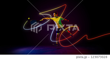 Tennis player in yellow shirt in motion with racket racket, with vibrant red and yellow neon light curves framing motion against dark background. 123073028