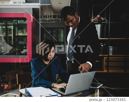 Businessman mentoring businesswoman in modern office, pointing at laptop screen while she focuses on work Businessman mentoring businesswoman in modern office, pointing at laptop screen while she focuses on work 123073381